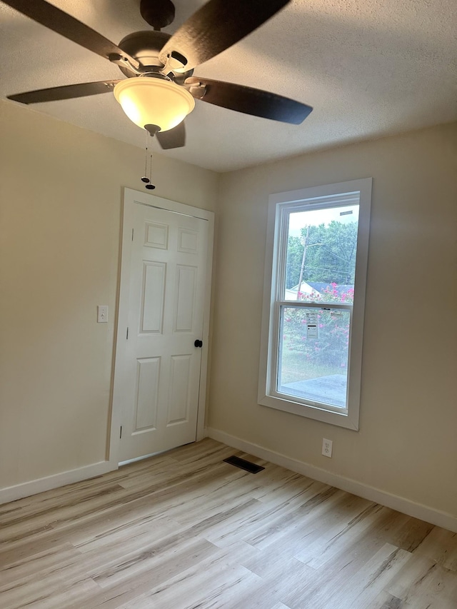 empty room with ceiling fan, light hardwood / wood-style floors, and a textured ceiling