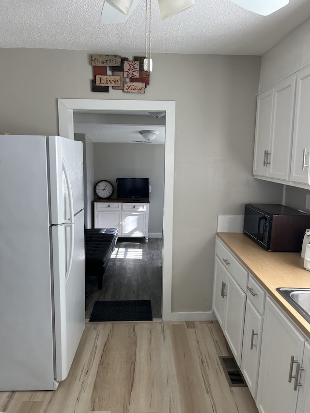 kitchen with white cabinetry, a textured ceiling, and white refrigerator