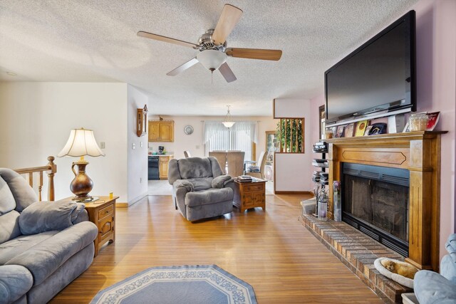 living room featuring a textured ceiling, light hardwood / wood-style flooring, a brick fireplace, and ceiling fan