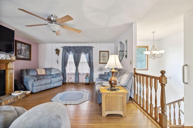 living room with a brick fireplace, a textured ceiling, hardwood / wood-style flooring, and ceiling fan with notable chandelier