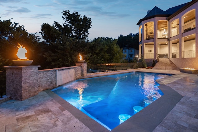 pool at dusk with pool water feature and a patio area