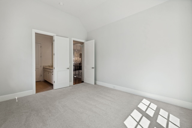 unfurnished bedroom featuring ensuite bathroom, light colored carpet, and vaulted ceiling