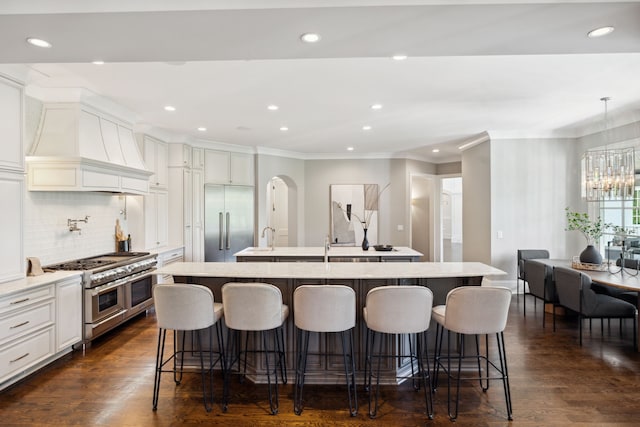 kitchen with premium appliances, a kitchen breakfast bar, custom range hood, dark wood-type flooring, and a center island with sink