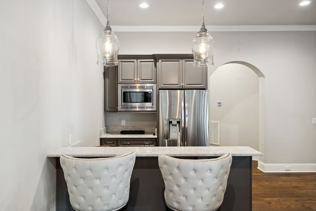 kitchen with appliances with stainless steel finishes, decorative light fixtures, dark hardwood / wood-style floors, and a kitchen breakfast bar