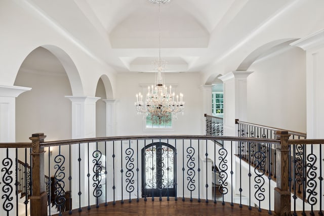 hall featuring a notable chandelier, ornate columns, and a raised ceiling