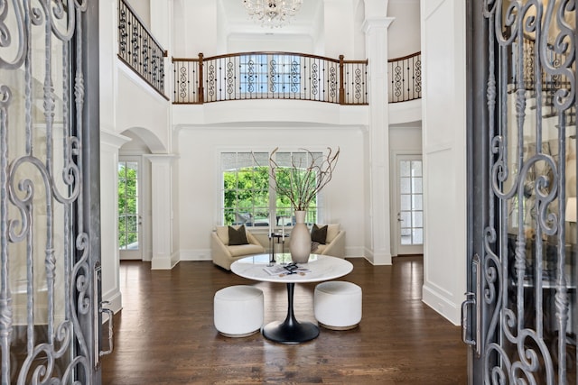 entrance foyer with dark wood-type flooring, ornate columns, a towering ceiling, and a chandelier