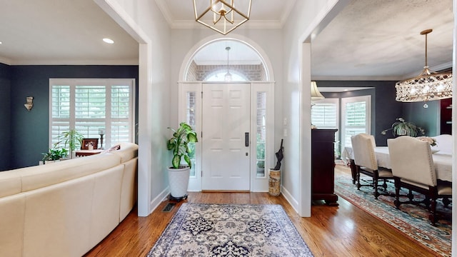 foyer entrance with ornamental molding, wood-type flooring, and a chandelier