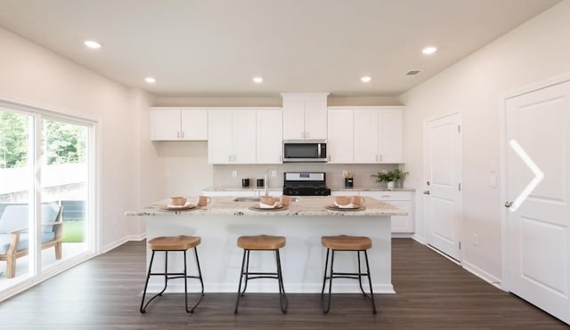 kitchen featuring stove, white cabinetry, a breakfast bar area, and an island with sink