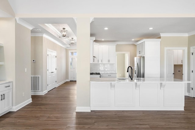 kitchen with stainless steel refrigerator with ice dispenser, a breakfast bar, sink, white cabinetry, and ornamental molding