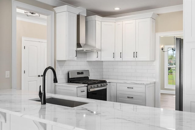 kitchen featuring stainless steel range with gas cooktop, white cabinetry, sink, light stone counters, and wall chimney range hood