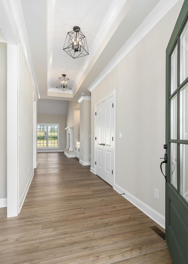 foyer featuring crown molding, a notable chandelier, hardwood / wood-style flooring, and a raised ceiling