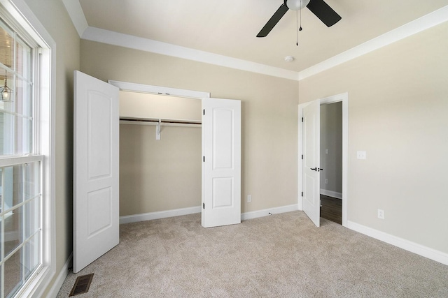 unfurnished bedroom featuring ceiling fan, a closet, ornamental molding, and light carpet