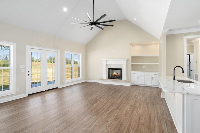 unfurnished living room with sink, high vaulted ceiling, ceiling fan, a high end fireplace, and hardwood / wood-style floors