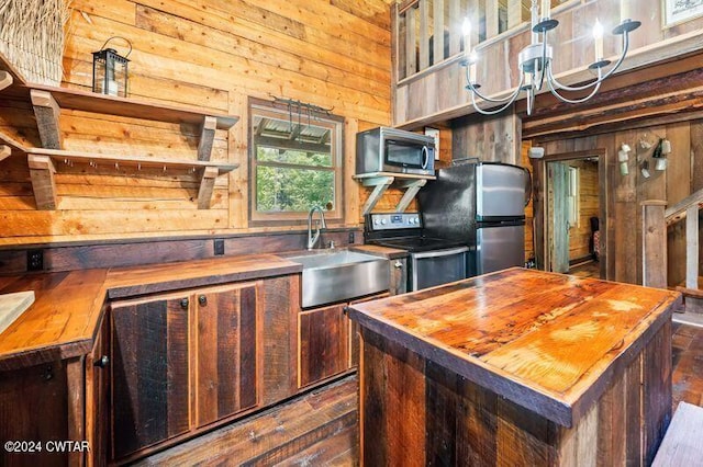 kitchen featuring sink, butcher block countertops, wood walls, a center island, and appliances with stainless steel finishes