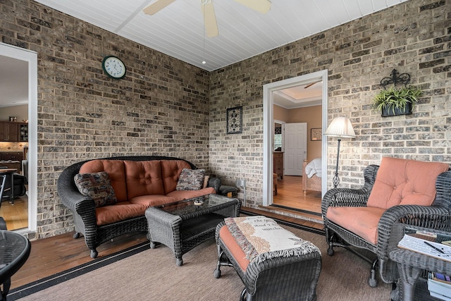 living room featuring hardwood / wood-style floors, ceiling fan, and brick wall