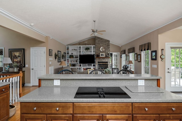 kitchen with vaulted ceiling, ornamental molding, a stone fireplace, and black electric cooktop