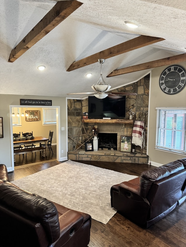 living room featuring hardwood / wood-style floors, a textured ceiling, a stone fireplace, and vaulted ceiling with beams