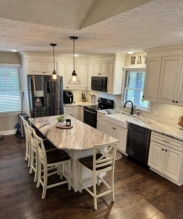 kitchen with black appliances, light stone counters, hanging light fixtures, a center island, and dark hardwood / wood-style flooring