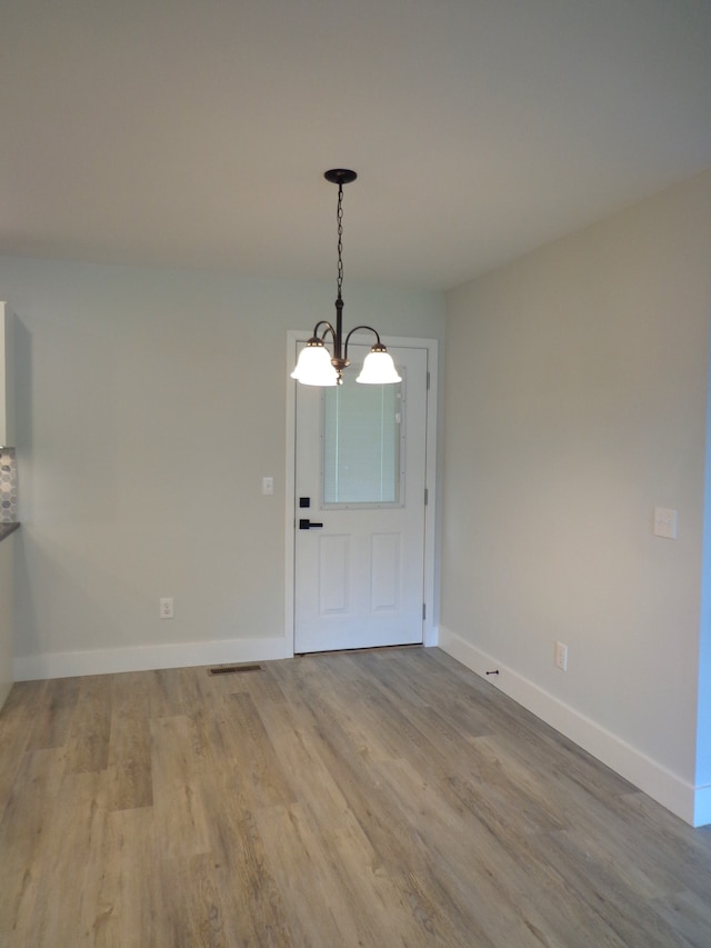 unfurnished dining area featuring an inviting chandelier and light hardwood / wood-style flooring