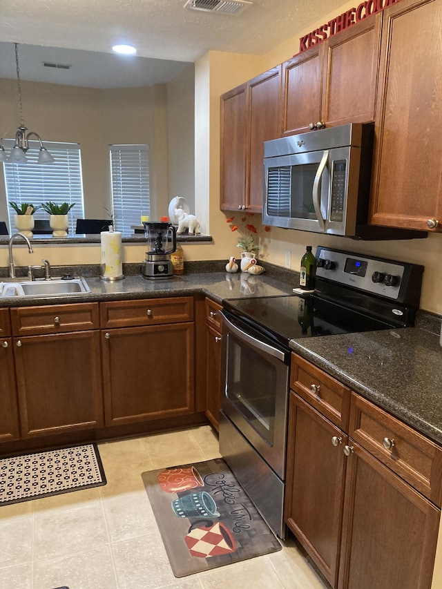 kitchen with stainless steel appliances, a peninsula, a sink, visible vents, and hanging light fixtures