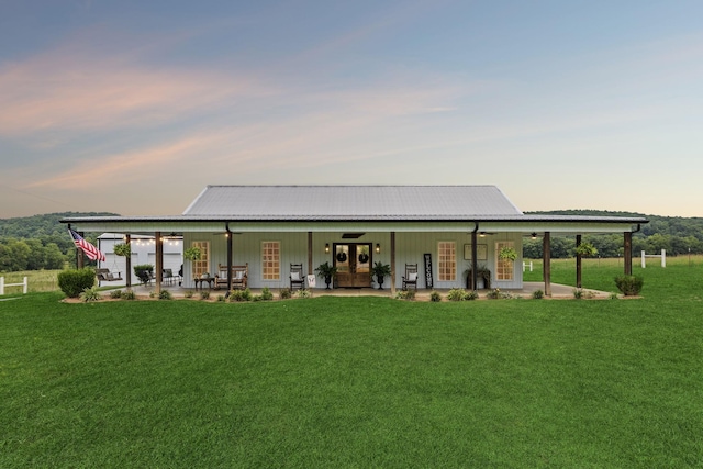 back house at dusk featuring covered porch and a lawn