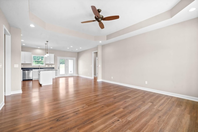 unfurnished living room with ceiling fan, sink, a raised ceiling, and hardwood / wood-style floors