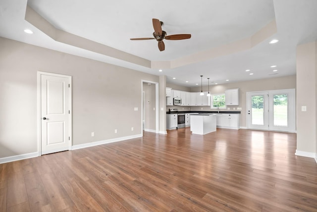 unfurnished living room featuring hardwood / wood-style floors, ceiling fan, and a tray ceiling