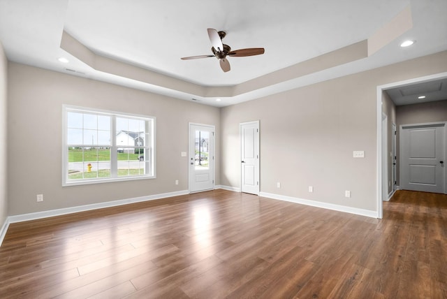 empty room with dark hardwood / wood-style floors, ceiling fan, and a tray ceiling