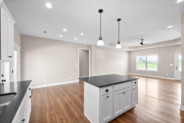 kitchen with ceiling fan, white cabinetry, hanging light fixtures, wood-type flooring, and a kitchen island