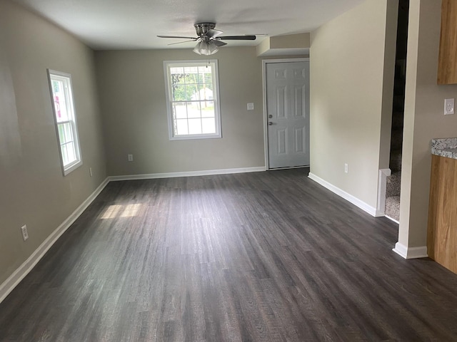 unfurnished living room with dark wood-style floors, a ceiling fan, and baseboards