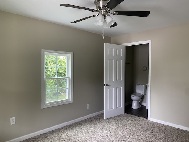 unfurnished bedroom featuring ceiling fan, dark carpet, and ensuite bathroom