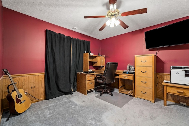 carpeted home office featuring ceiling fan, a textured ceiling, and wood walls