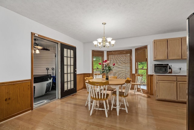 dining room featuring a chandelier, light wood-type flooring, wooden walls, and a textured ceiling