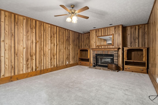 unfurnished living room featuring ceiling fan, wooden walls, a fireplace, a textured ceiling, and light carpet