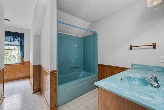 bathroom with vanity, a textured ceiling, vaulted ceiling, shower / bathtub combination, and wood walls