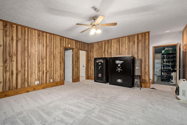 unfurnished bedroom featuring ceiling fan, light colored carpet, a textured ceiling, and wooden walls