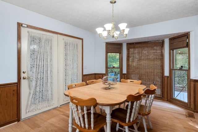 dining room featuring a notable chandelier, wood walls, a textured ceiling, and light hardwood / wood-style flooring