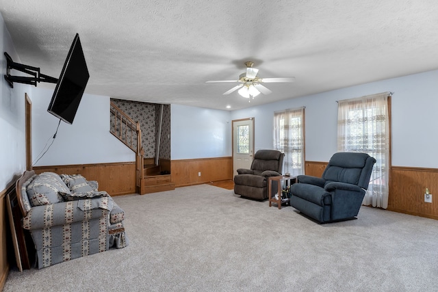 carpeted living room with ceiling fan, wooden walls, and a textured ceiling