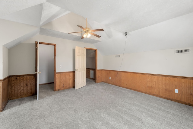 bonus room with vaulted ceiling, a textured ceiling, ceiling fan, wooden walls, and light colored carpet