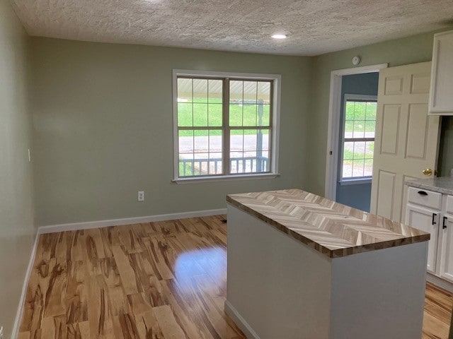 kitchen with white cabinets, light wood-type flooring, a center island, and a textured ceiling