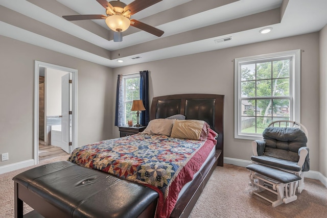 bedroom featuring ensuite bathroom, a raised ceiling, and light carpet