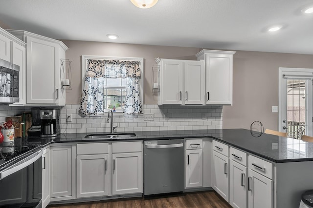 kitchen with appliances with stainless steel finishes, sink, white cabinets, kitchen peninsula, and plenty of natural light