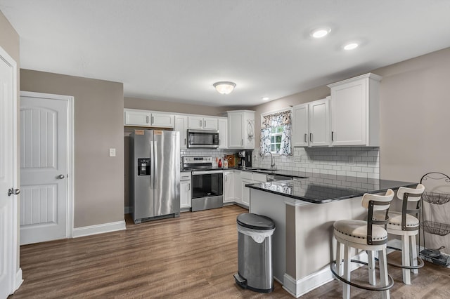 kitchen featuring sink, appliances with stainless steel finishes, white cabinetry, a kitchen breakfast bar, and kitchen peninsula