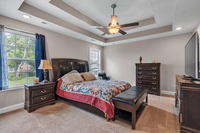 bedroom with multiple windows, a tray ceiling, light carpet, and ceiling fan