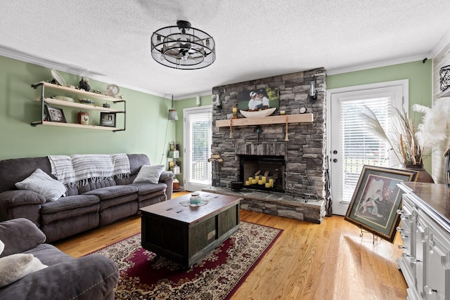 living room with crown molding, a stone fireplace, light hardwood / wood-style floors, and a textured ceiling