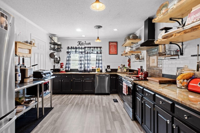 kitchen with pendant lighting, wall chimney range hood, crown molding, stainless steel appliances, and light stone counters