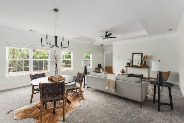 carpeted living room with crown molding, ceiling fan with notable chandelier, a tray ceiling, and a healthy amount of sunlight