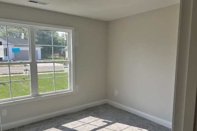 carpeted spare room featuring a healthy amount of sunlight, baseboards, and visible vents