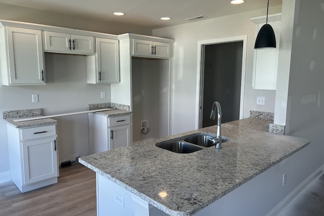 kitchen featuring a peninsula, light stone counters, a sink, and recessed lighting