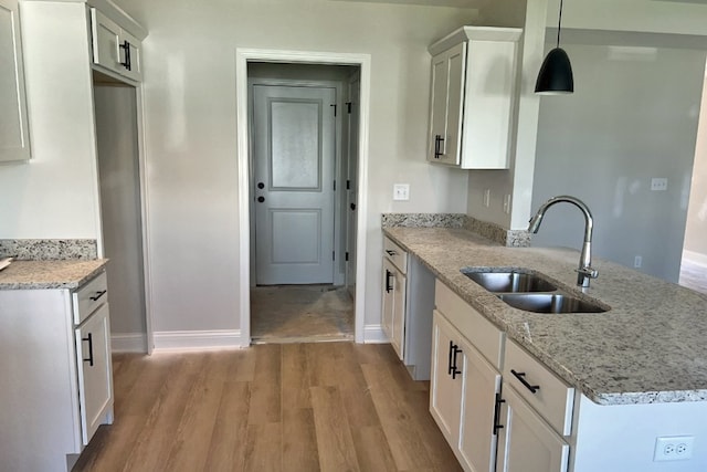 kitchen with light stone countertops, light wood finished floors, white cabinets, and a sink